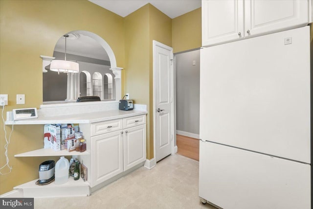 kitchen featuring freestanding refrigerator, light floors, light countertops, white cabinetry, and arched walkways