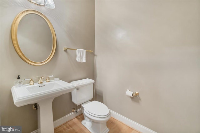 half bath featuring baseboards, wood finished floors, and toilet