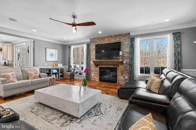 living room with ornamental molding, wood finished floors, a stone fireplace, ceiling fan, and recessed lighting