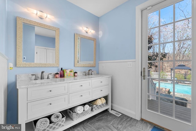 full bath with a wainscoted wall, visible vents, a sink, and double vanity