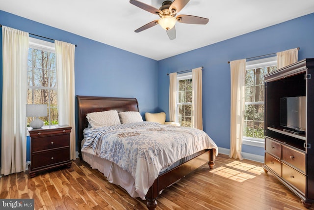 bedroom with a ceiling fan, baseboards, multiple windows, and wood finished floors