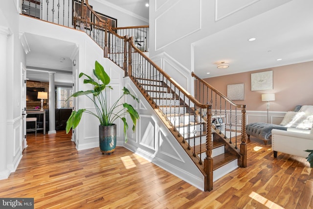stairway featuring ornate columns, a decorative wall, ornamental molding, and wood finished floors
