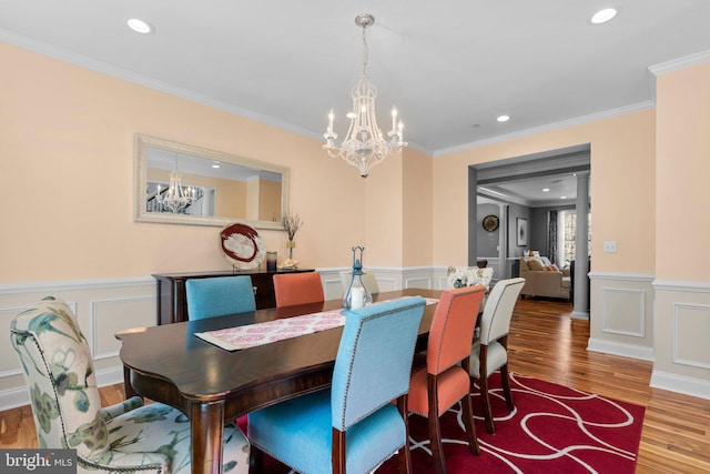 dining space featuring ornamental molding, a decorative wall, a notable chandelier, and wood finished floors