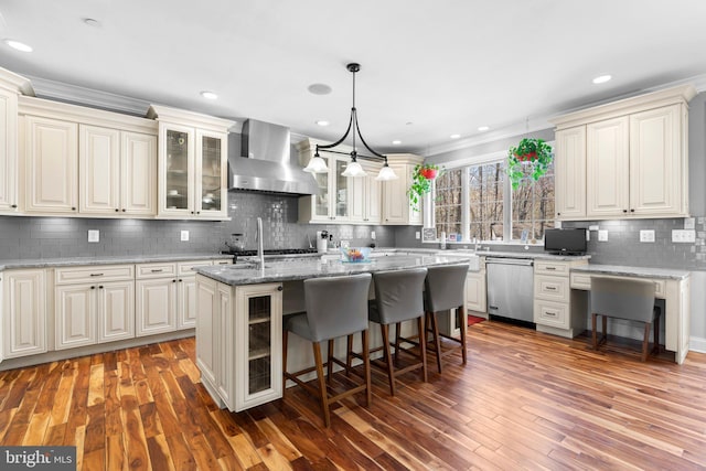 kitchen with an island with sink, wall chimney exhaust hood, light stone countertops, a breakfast bar, and stainless steel appliances