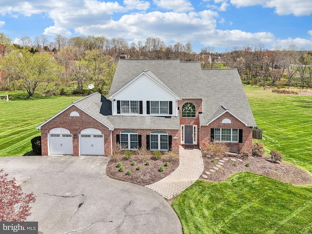 view of front facade with an attached garage, driveway, a front lawn, and brick siding
