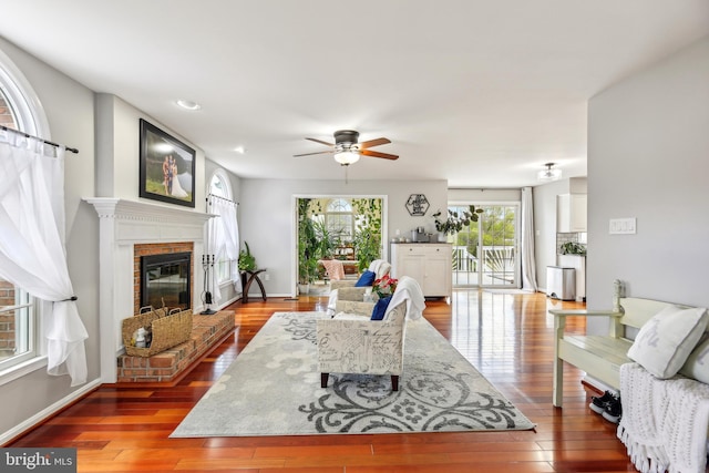 living area with ceiling fan, recessed lighting, wood-type flooring, a brick fireplace, and baseboards
