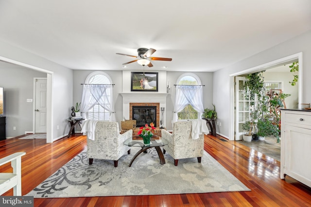 living area with wood-type flooring, ceiling fan, baseboards, and a fireplace