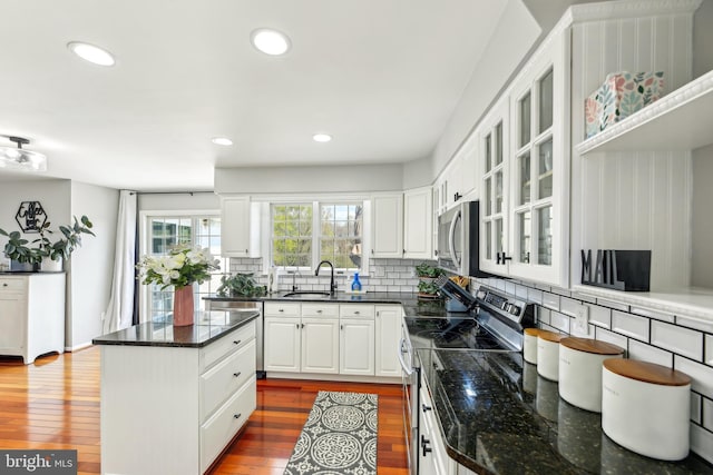 kitchen with appliances with stainless steel finishes, glass insert cabinets, white cabinets, decorative backsplash, and a sink