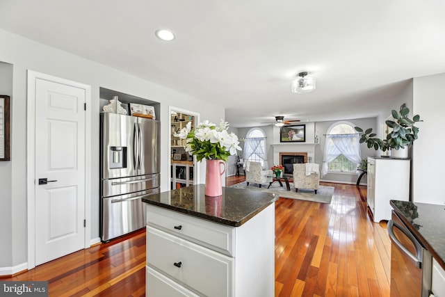 kitchen with stainless steel fridge with ice dispenser, white cabinets, a brick fireplace, ceiling fan, and hardwood / wood-style flooring