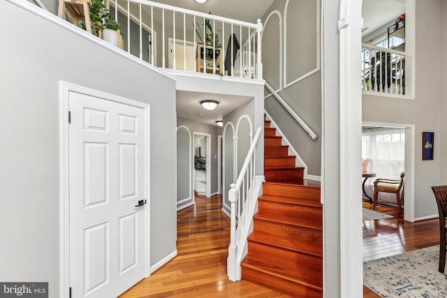 staircase with arched walkways, wood-type flooring, baseboards, and a towering ceiling