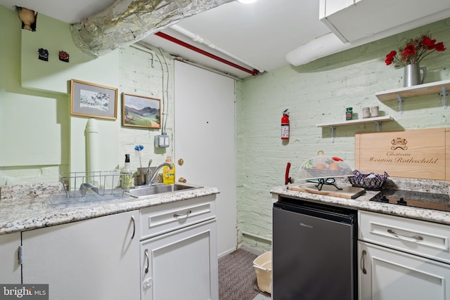 kitchen featuring fridge, black electric cooktop, white cabinets, a sink, and carpet