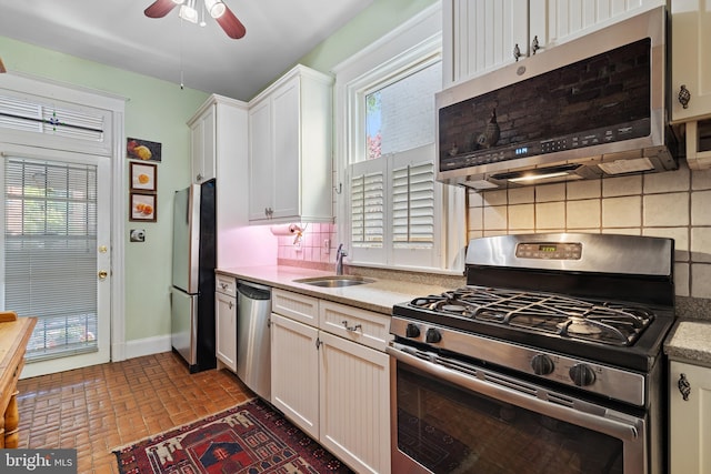 kitchen featuring ceiling fan, appliances with stainless steel finishes, a sink, brick floor, and light countertops