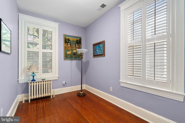 empty room featuring radiator heating unit, baseboards, dark wood-type flooring, and visible vents