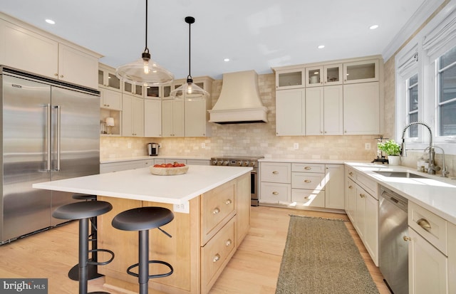 kitchen featuring premium appliances, premium range hood, a sink, a center island, and a breakfast bar area