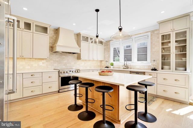 kitchen with stainless steel electric range, custom range hood, a breakfast bar, light countertops, and light wood-style flooring