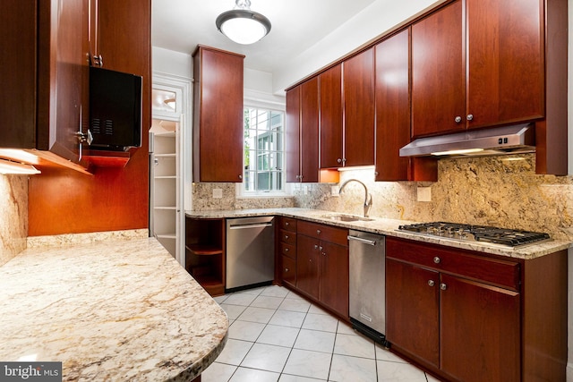kitchen featuring light stone countertops, under cabinet range hood, tasteful backsplash, a sink, and appliances with stainless steel finishes