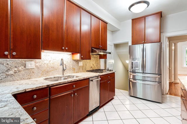 kitchen with decorative backsplash, under cabinet range hood, light stone counters, a sink, and appliances with stainless steel finishes