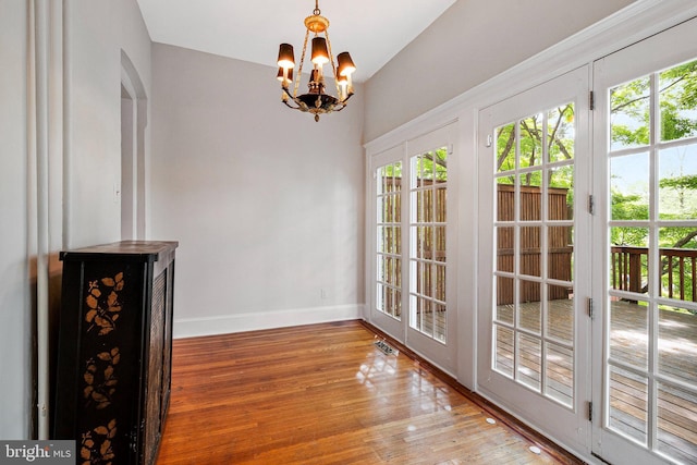 unfurnished dining area featuring baseboards, a chandelier, wood finished floors, and a wealth of natural light