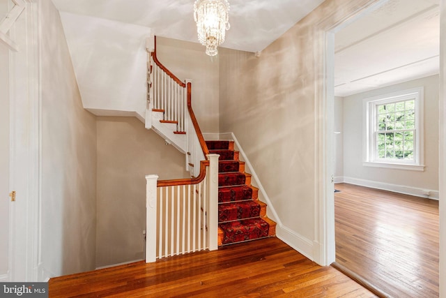 staircase with an inviting chandelier, baseboards, and hardwood / wood-style floors