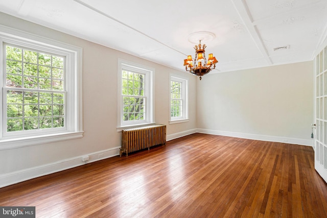 spare room with an inviting chandelier, radiator heating unit, hardwood / wood-style floors, baseboards, and visible vents