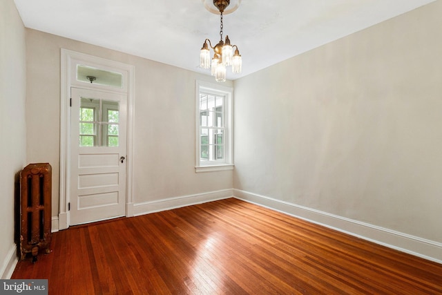 unfurnished dining area with wood finished floors, baseboards, radiator heating unit, and a chandelier