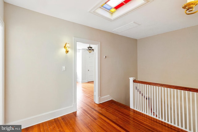 corridor with visible vents, hardwood / wood-style floors, baseboards, an upstairs landing, and a skylight