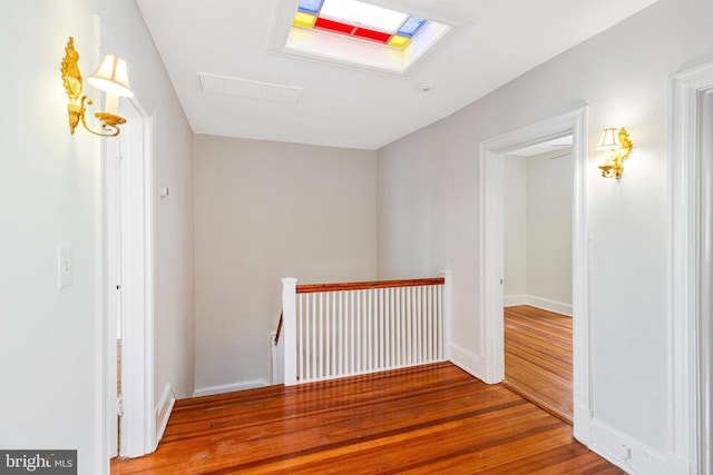 hall featuring visible vents, a skylight, wood finished floors, baseboards, and an upstairs landing