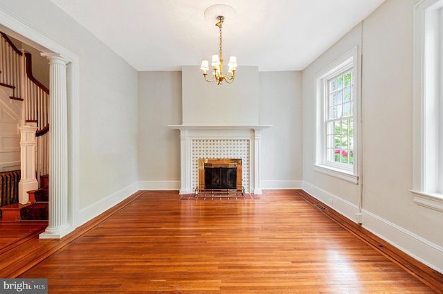 unfurnished living room with a tile fireplace, baseboards, a chandelier, stairs, and light wood-style flooring
