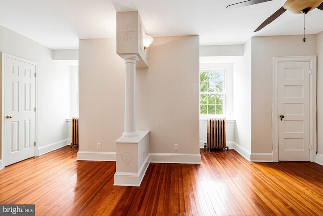 interior space with baseboards, radiator heating unit, ornate columns, hardwood / wood-style flooring, and a ceiling fan