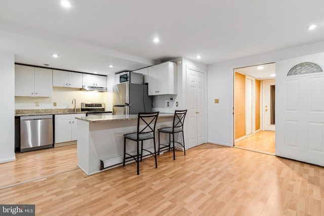 kitchen featuring a sink, a peninsula, light wood finished floors, stainless steel appliances, and white cabinetry