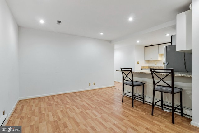 kitchen featuring a breakfast bar, light wood-style floors, freestanding refrigerator, white cabinetry, and a peninsula