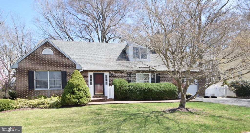 view of front of home featuring a front yard, a shingled roof, fence, concrete driveway, and brick siding