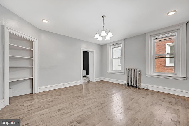 unfurnished dining area with an inviting chandelier, radiator heating unit, wood finished floors, and baseboards