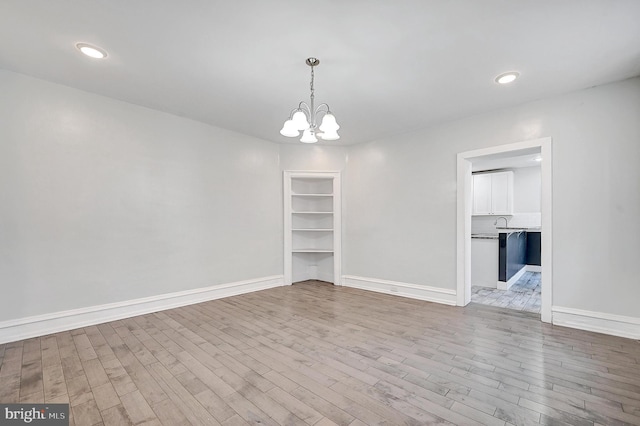 unfurnished dining area featuring baseboards, recessed lighting, wood finished floors, and an inviting chandelier