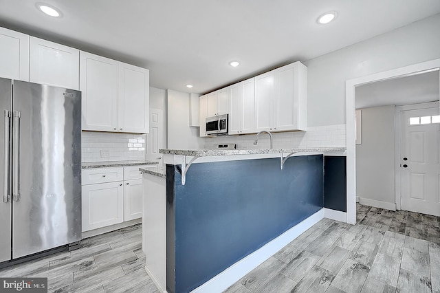 kitchen with light stone countertops, white cabinets, appliances with stainless steel finishes, and tasteful backsplash