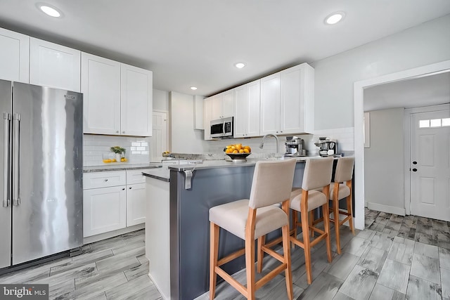 kitchen with backsplash, a kitchen breakfast bar, white cabinets, and appliances with stainless steel finishes