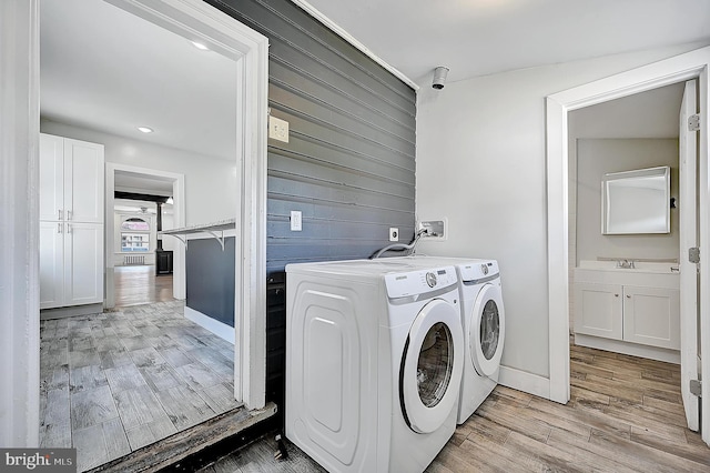 laundry room featuring laundry area, wood walls, light wood finished floors, a sink, and washing machine and dryer