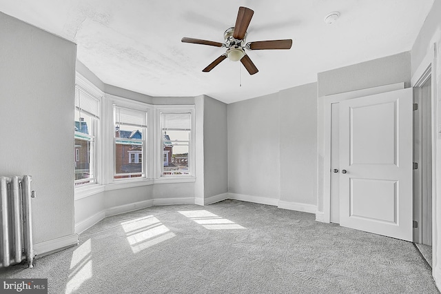 unfurnished bedroom with radiator heating unit, a ceiling fan, carpet flooring, and baseboards