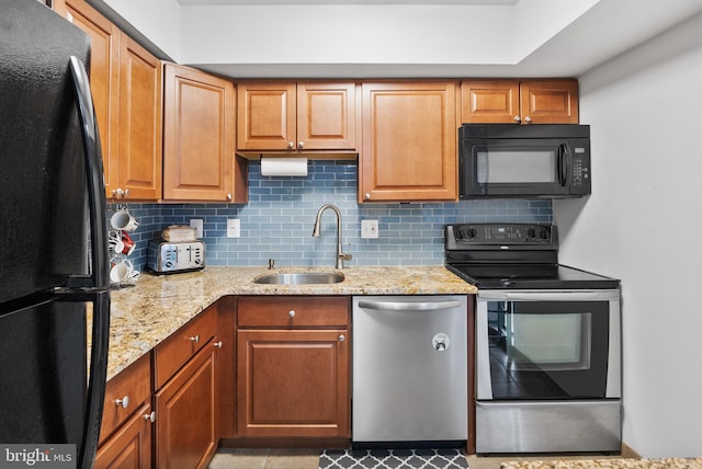 kitchen with tasteful backsplash, a sink, brown cabinets, black appliances, and light stone counters