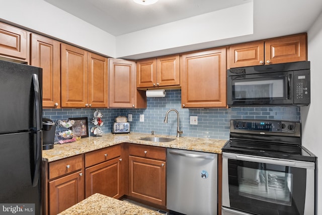 kitchen with light stone counters, backsplash, black appliances, brown cabinets, and a sink