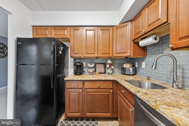 kitchen featuring a sink, freestanding refrigerator, decorative backsplash, stainless steel dishwasher, and light stone counters