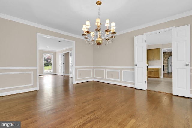 unfurnished dining area featuring ornamental molding, wood finished floors, and a notable chandelier
