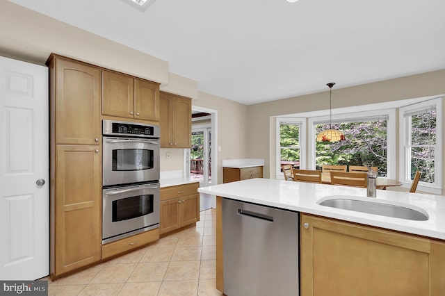 kitchen featuring decorative light fixtures, appliances with stainless steel finishes, a sink, light tile patterned floors, and light countertops
