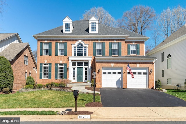 colonial house featuring brick siding, aphalt driveway, a garage, roof with shingles, and a front lawn