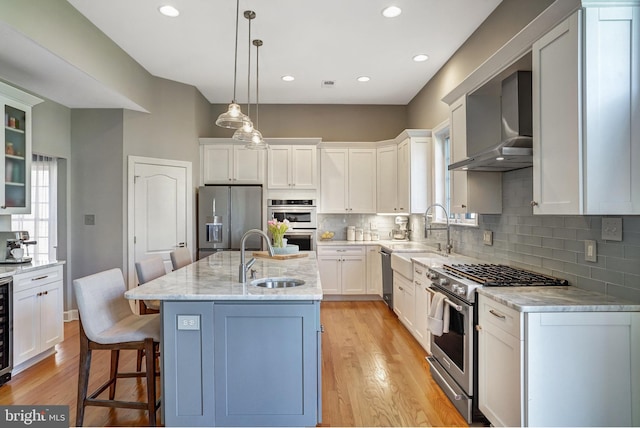 kitchen featuring light wood-style flooring, stainless steel appliances, a sink, and wall chimney exhaust hood