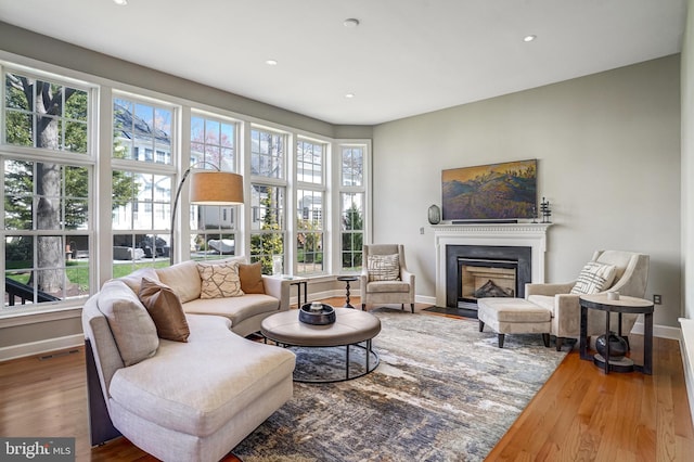 living area with baseboards, recessed lighting, a fireplace with flush hearth, and wood finished floors