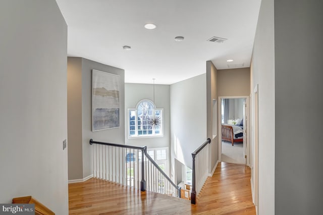 hall with wood finished floors, visible vents, an upstairs landing, and a notable chandelier
