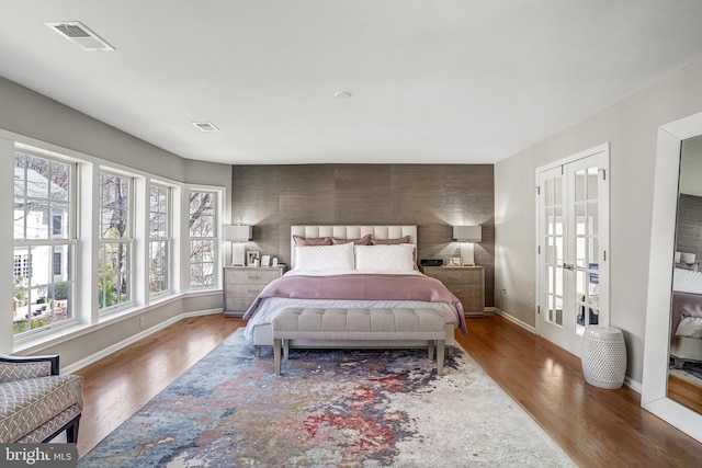 bedroom with baseboards, french doors, visible vents, and wood finished floors