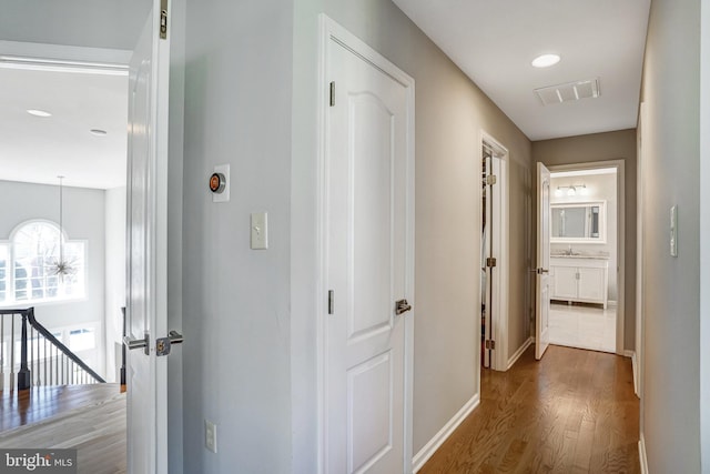 hallway featuring wood finished floors, baseboards, an upstairs landing, recessed lighting, and a chandelier