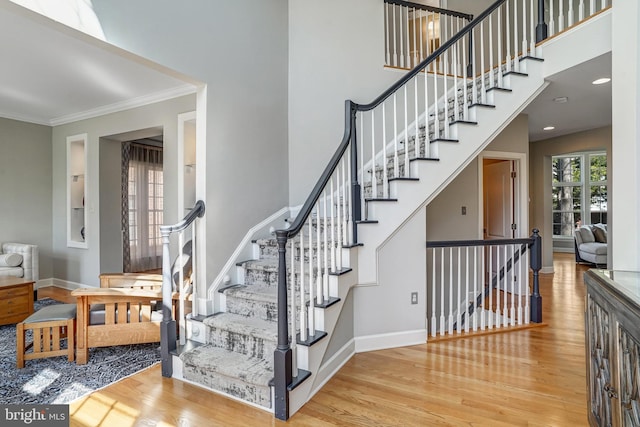 stairway with ornamental molding, baseboards, a towering ceiling, and wood finished floors